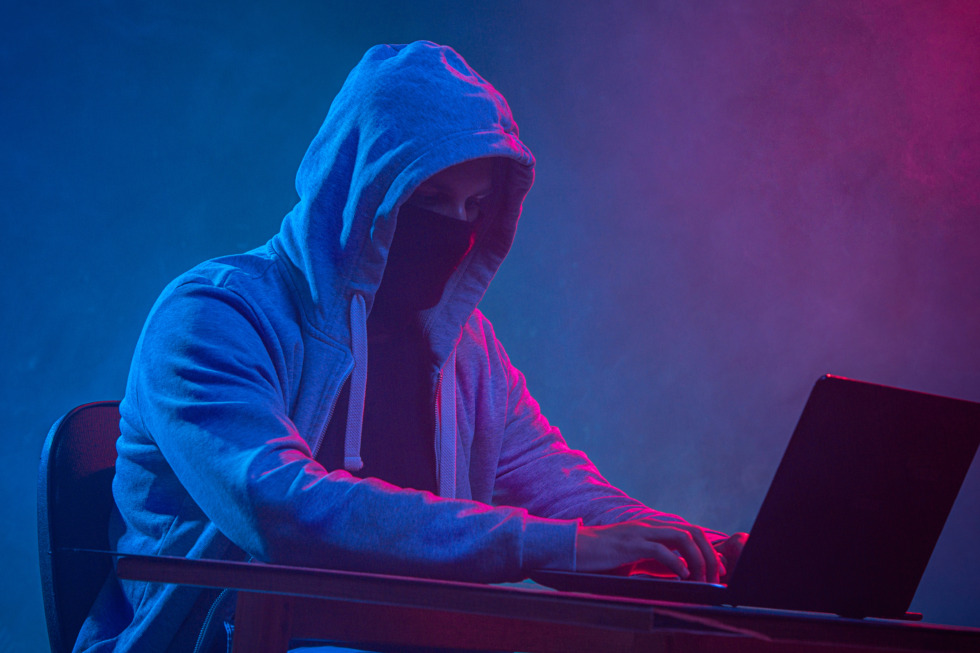 hooded computer hacker stealing information with laptop